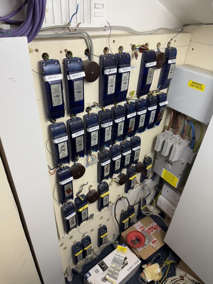 A wall of failed blue Rako lighting control modules, more than thirty circuits, with loose wiring and boxes of spare parts on the floor