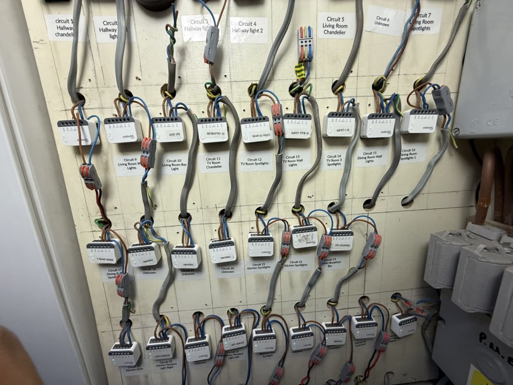 A wall of white Zigbee relay modules, each circuit labelled with the room it controls