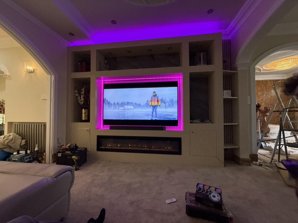 A finished media wall with a large television, cove lighting and a linear fireplace