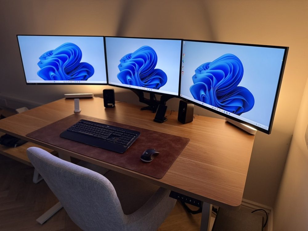 A three-monitor trading desk on a single clamped arm, lit by a warm light bar